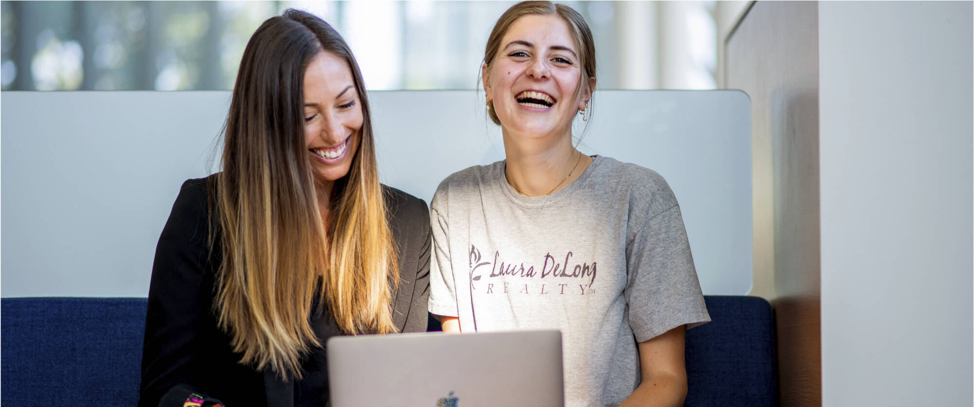 Two smiling women sitting sharing a laptop